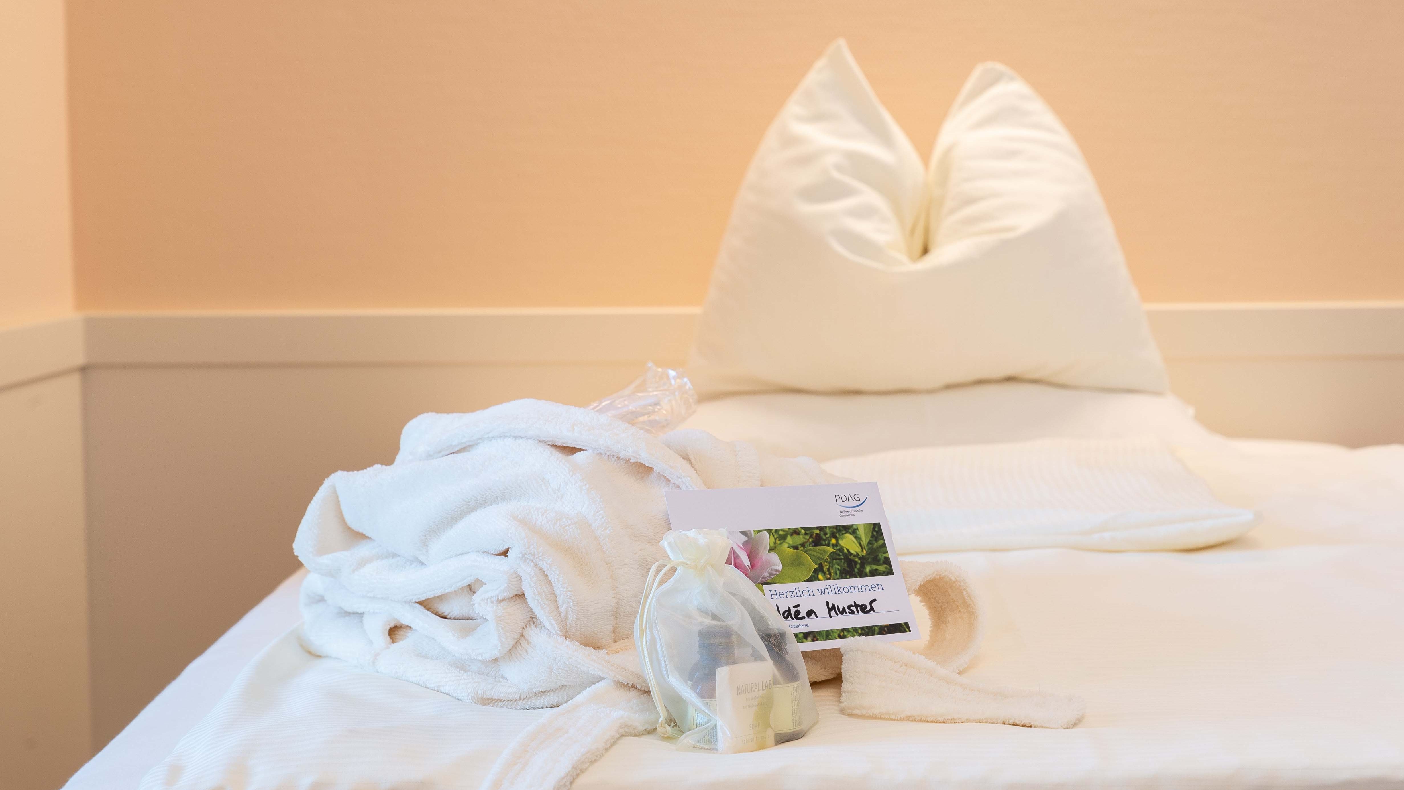 Ein Bett auf dem ein schön gefalteter Bademantel und ein Geschenkbeutel mit Pflegeartikeln liegen 