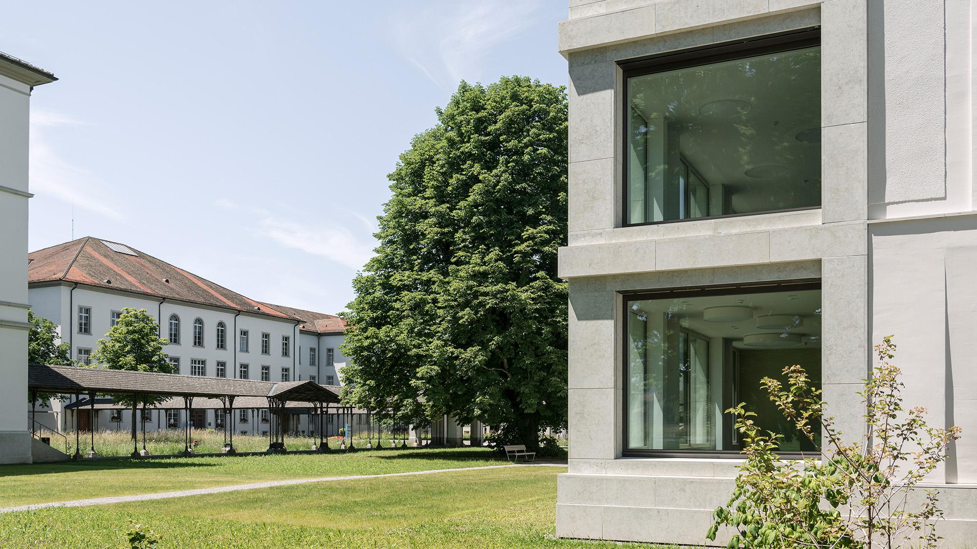 Zwischen dem modernen Neubau mit seinen bodentiefen Fenstern und dem historischen Gebäude mit seiner weissen Fassade steht ein über 15 Meter grosser Baum