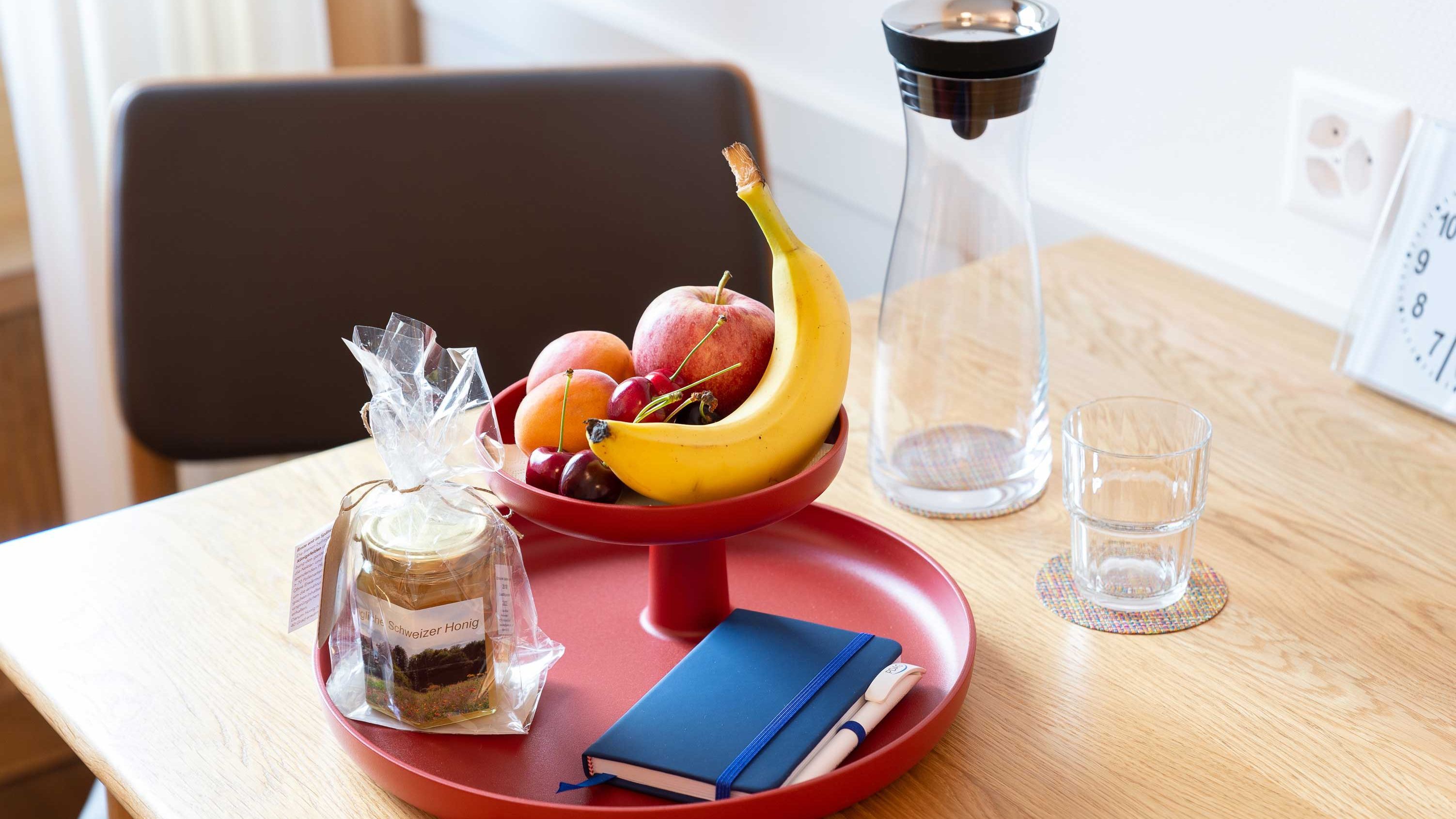 Ein Tisch mit Trinkwasserkaraffe, frischen Früchten und einem Geschenkset