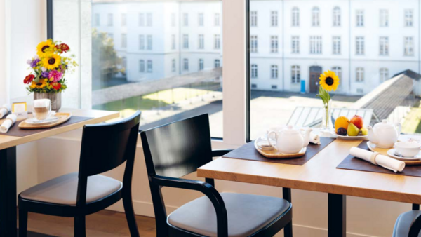 Gedeckte Tische im Speisesaal mit Früchten, Teeset, Cappuccino und Blumenstrauss