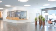 Das helle, lichtdurchflutete Foyer mit grossen Blumentöpfen und dem Empfangsschalter für Patientinnen und Patienten