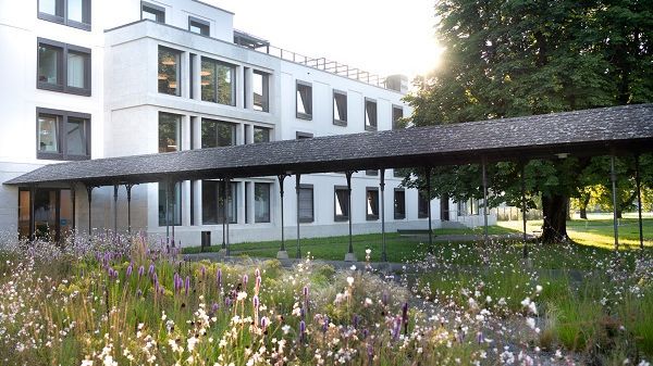 Die moderne Fassade des Gebäude Magnolia der PDAG, davor ein grosser grüner Baum und eine blühende Wiese