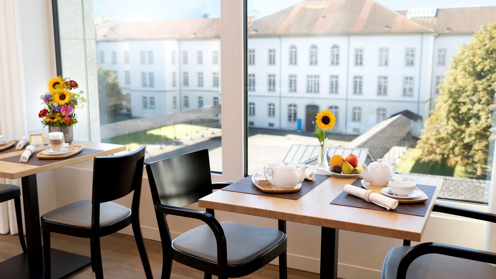 Zwei gedeckte Tische mit Blumendekoration und daneben weite Fenster die das historische Gebäude der Klinik Königsfelden zeigen