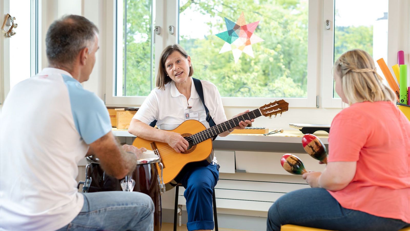 Eine Therapeutin spielt Gitarre und wird von zwei Patienten mit Trommel und Rassel begleitet