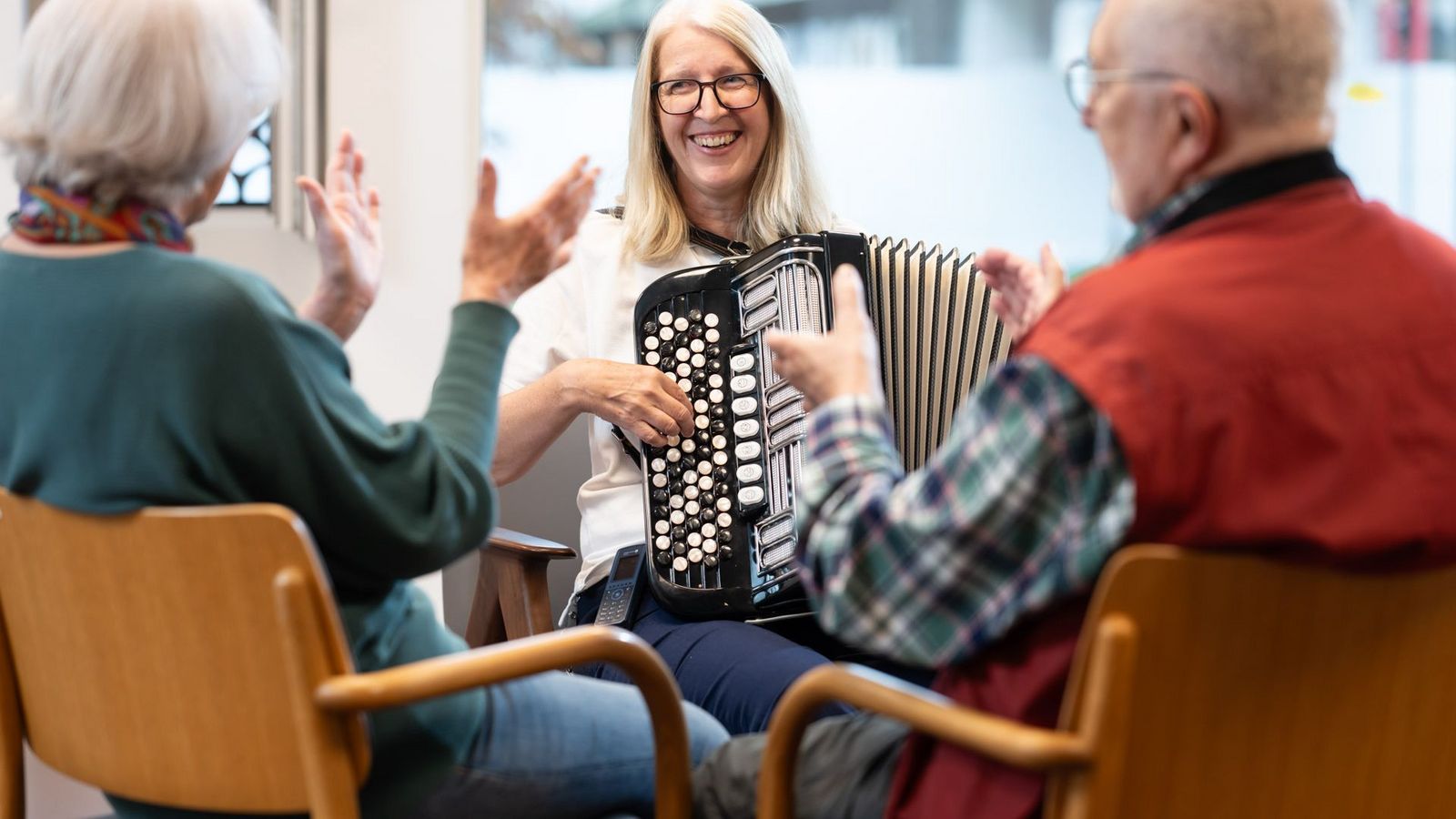 Eine Therapeutin spielt lächelnd Akkordeon, während die Patienten mitklatschen