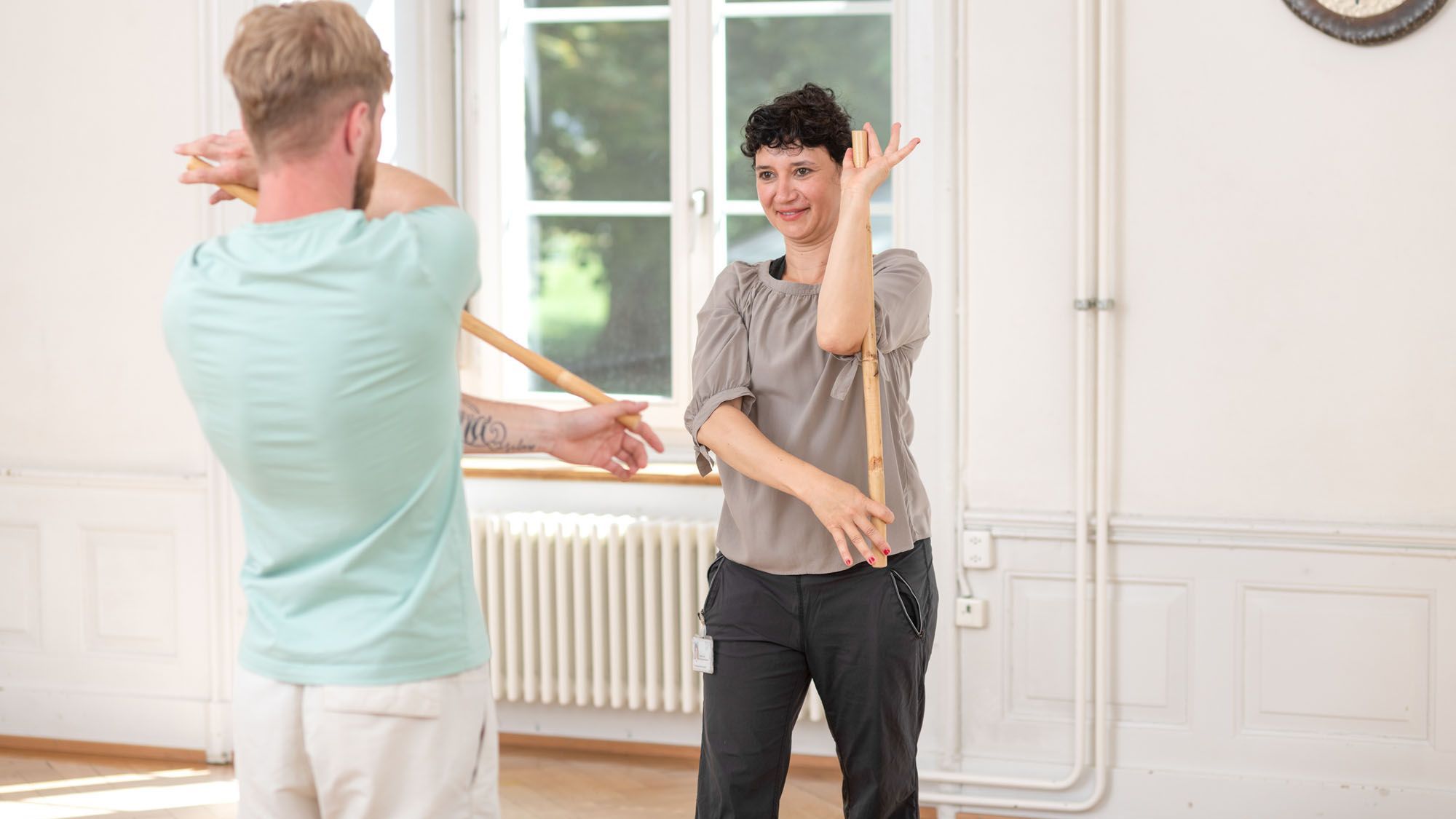 Die Therapeutin zeigt eine Übung mit einem Fitnessstab vor