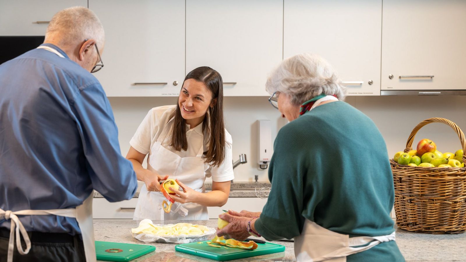 Eine Therapeutin und zwei Patienten schälen in der Küche Äpfel