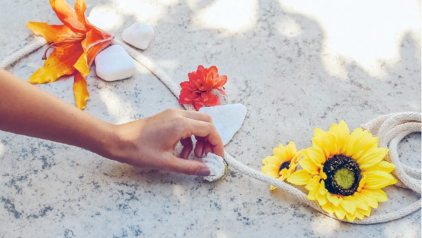 Eine Hand platziert eine Muscheln auf dem Boden neben Blumen und Steinen