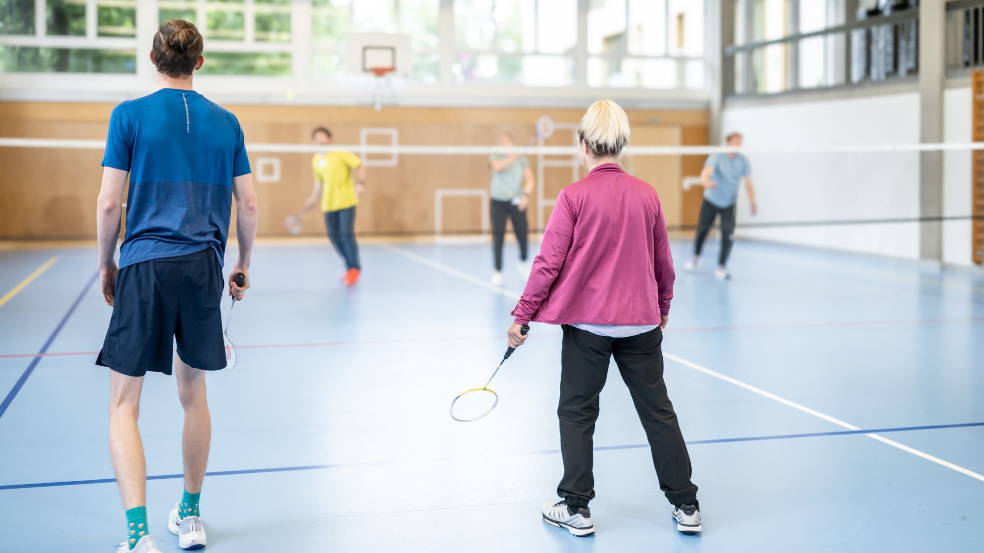 Ein Patient und eine Patientin spielen in einer Turnhalle Badminton
