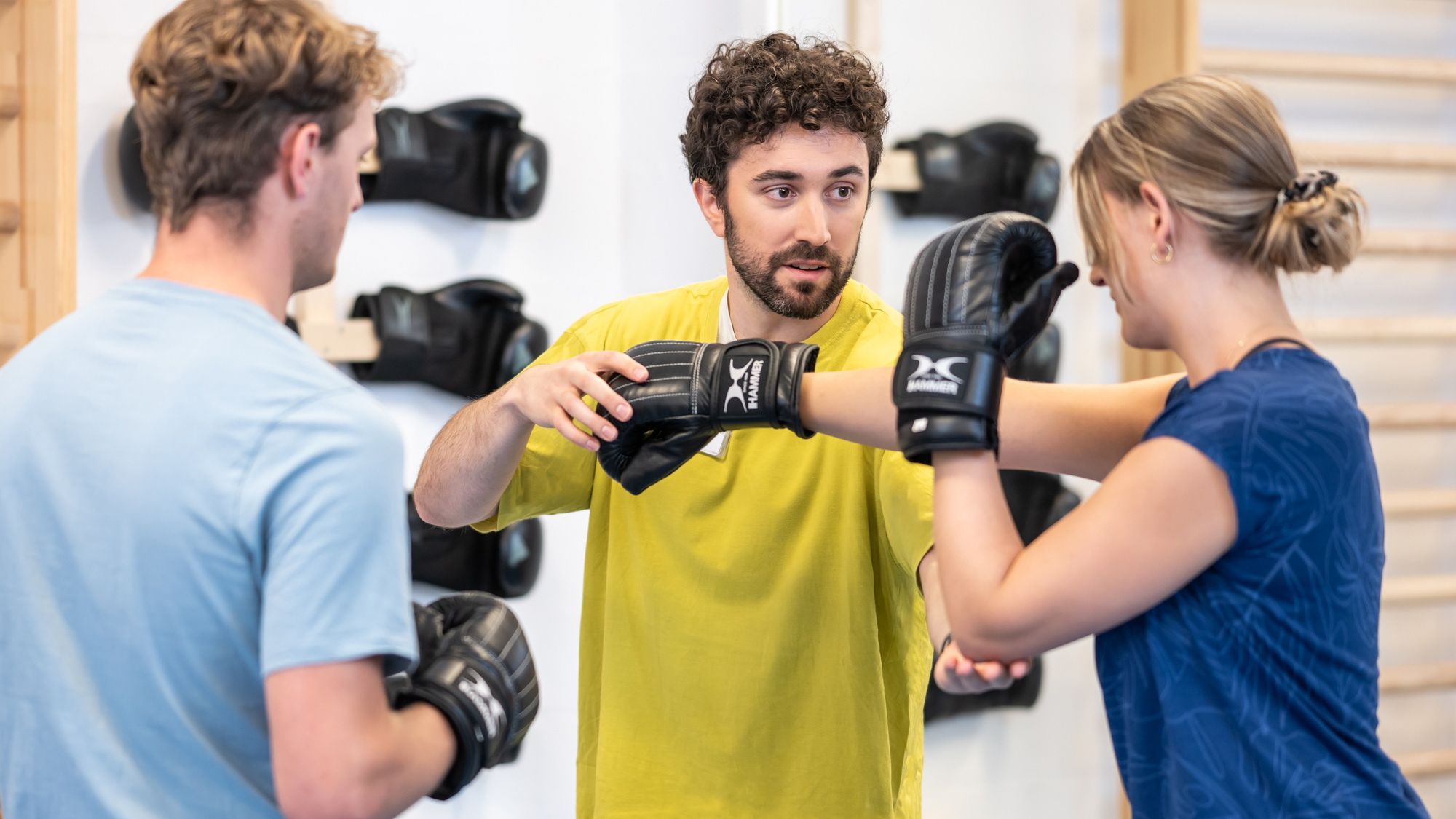 Ein Sporttherapeut zeigt einer Patientin die richtige Bewegung beim Boxen