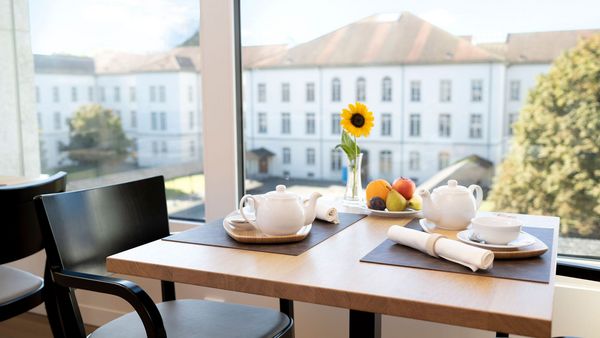 Ein gedeckter Esstisch mit Sonnenblume und Ausblick durchs Fenster auf das historische Klinikgebäude Königsfelden